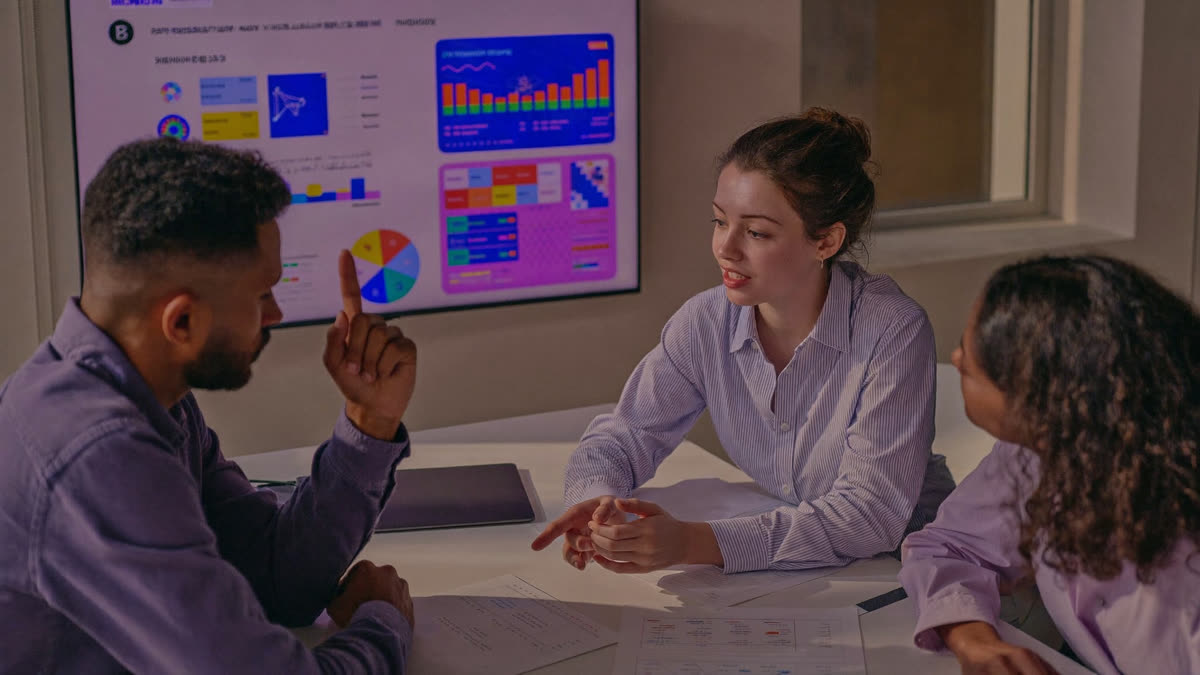 A small marketing team discusses audience charts on a wall screen