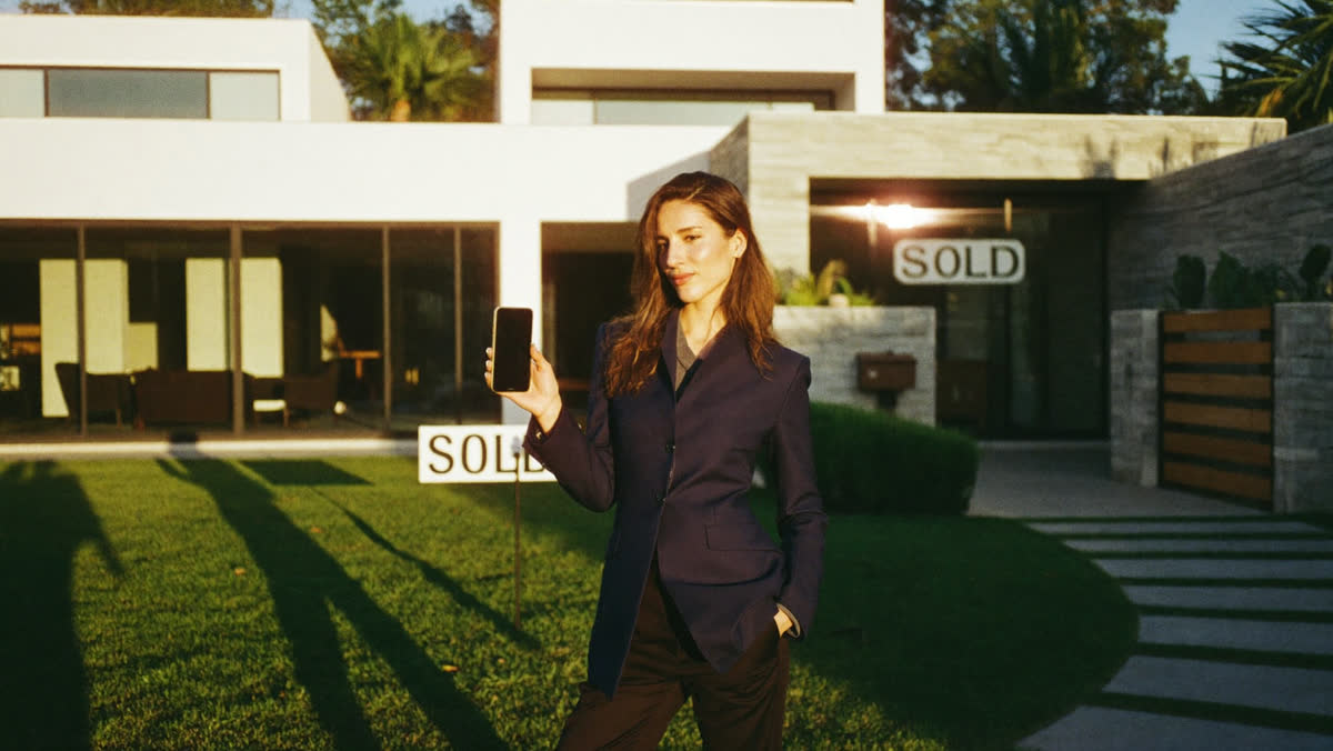 Real estate agent with a phone in front of a sold home
